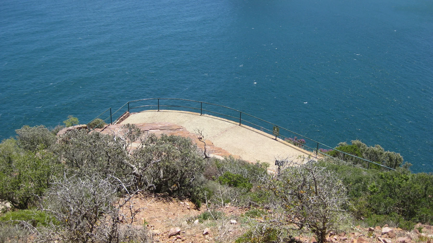 A paved lookout with railings sits below the viewpoint above open blue water.