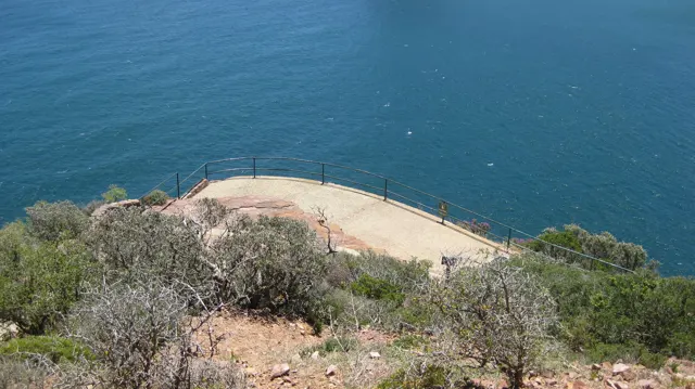A paved lookout with railings sits below the viewpoint above open blue water.