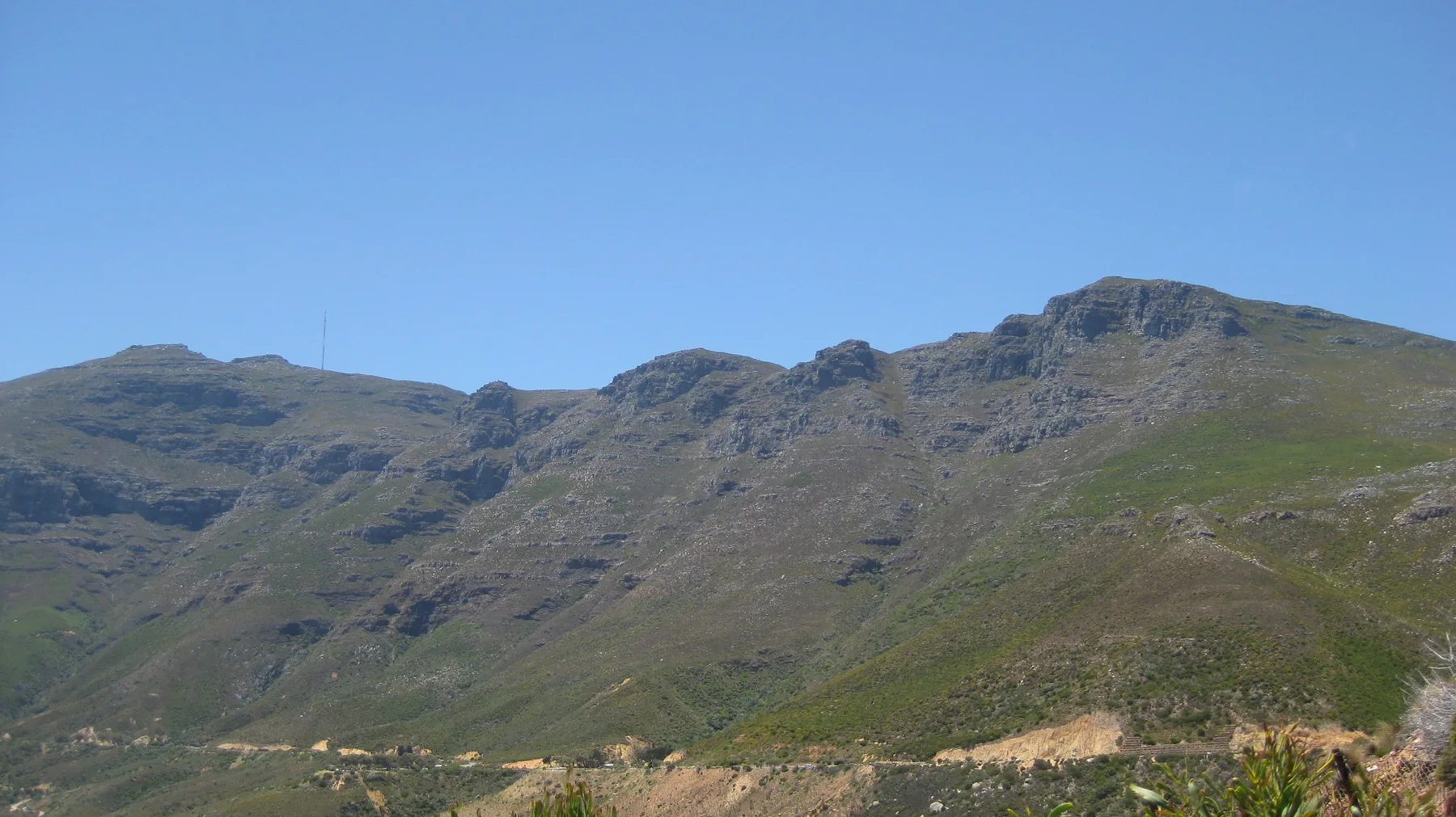 Rugged green mountain ridges stand beneath a clear blue sky.
