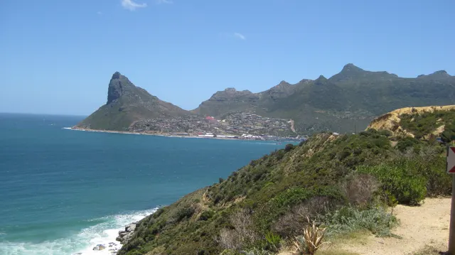 A sharply sloping headland rises across blue water beyond low coastal greenery.