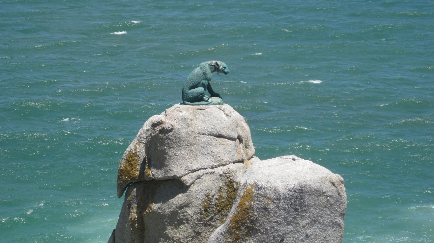 A small green sculpture of a seated figure rests on a pale rock offshore.