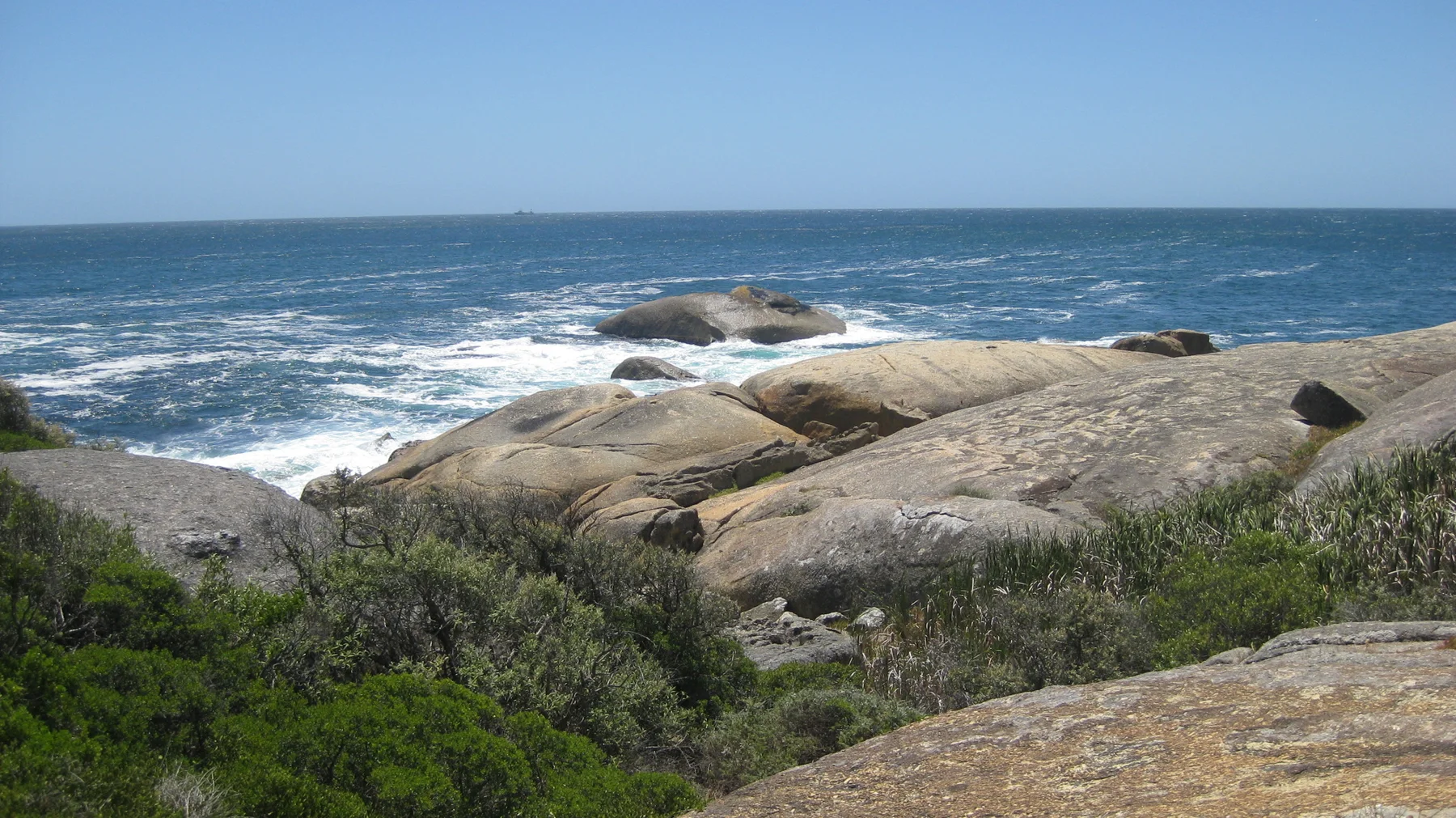 Smooth rounded boulders and dark vegetation frame white waves along the shore.