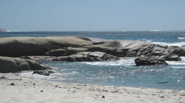 Rounded boulders enclose a small blue pool beside pale sand.