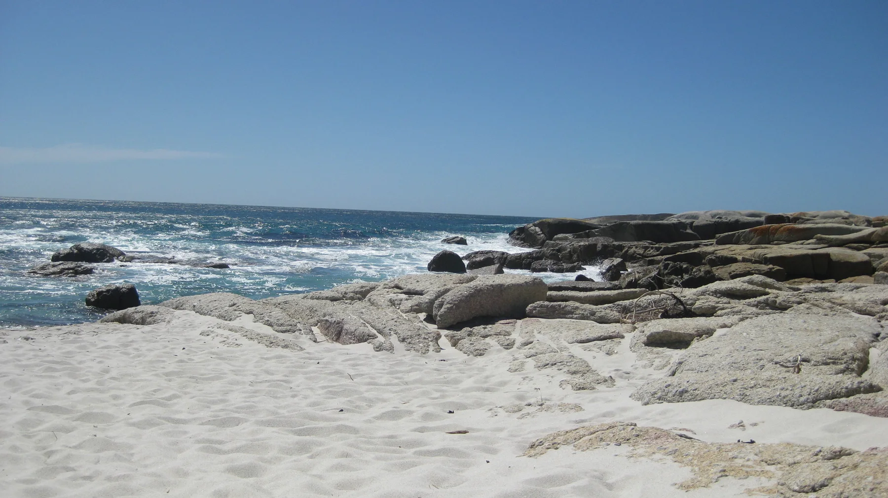 A white sandy cove curves past rounded rocks toward the blue ocean.