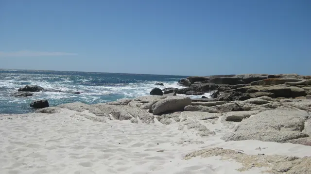A white sandy cove curves past rounded rocks toward the blue ocean.