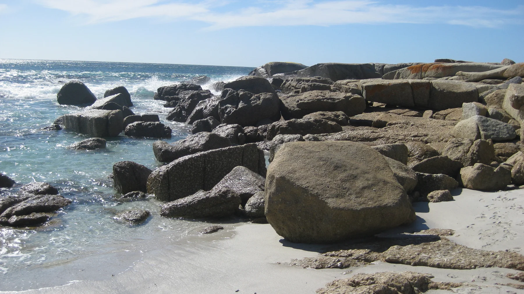 Large rounded boulders lie scattered across shallow water and pale sand.