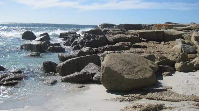 Large rounded boulders lie scattered across shallow water and pale sand.