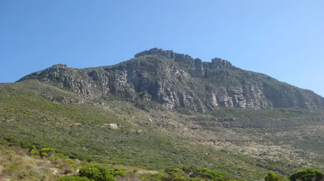 A broad rocky ridge rises above a green slope beneath clear blue sky.