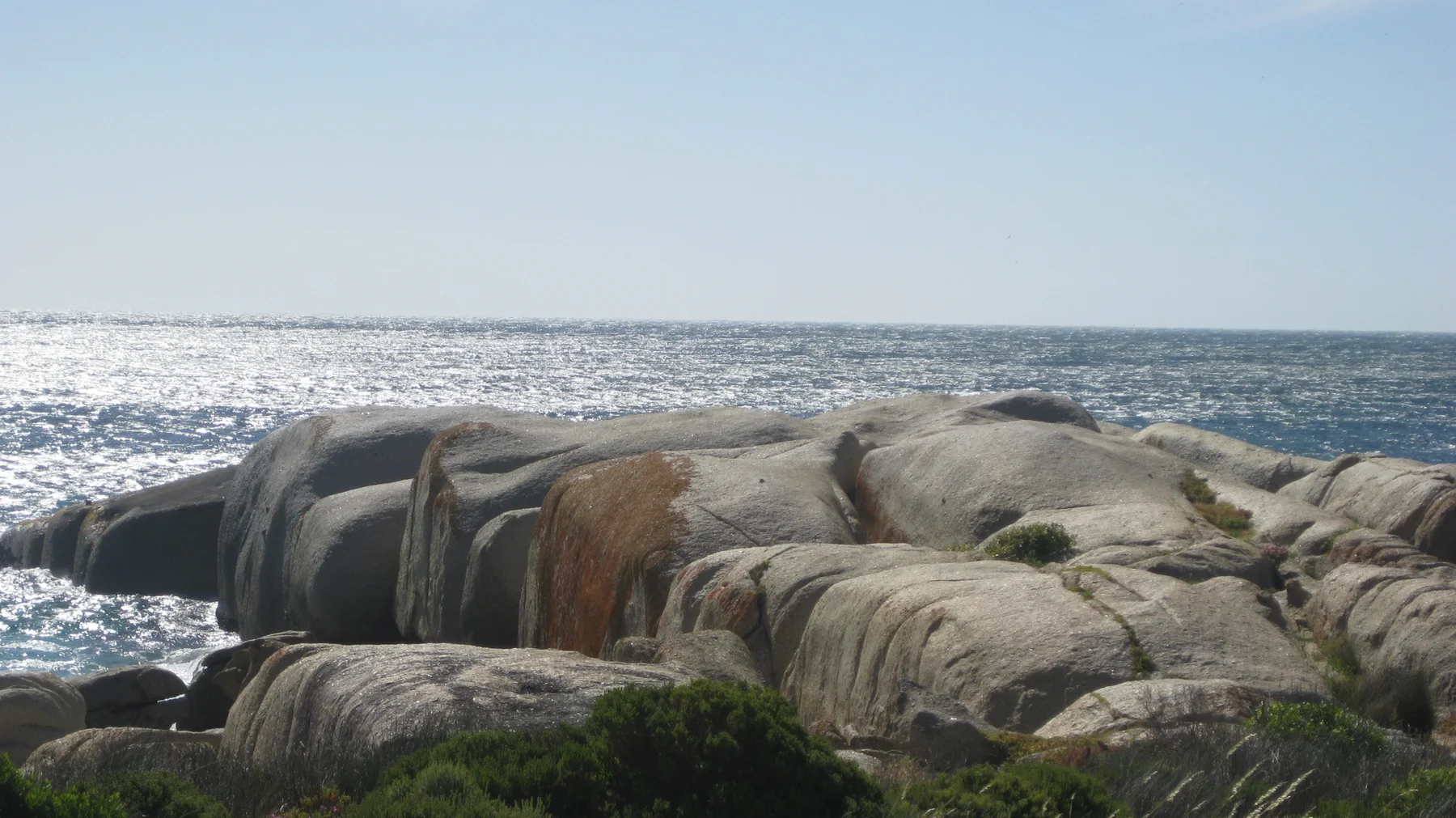 Rounded brown and grey boulders stand against a stretch of sunlit sea.