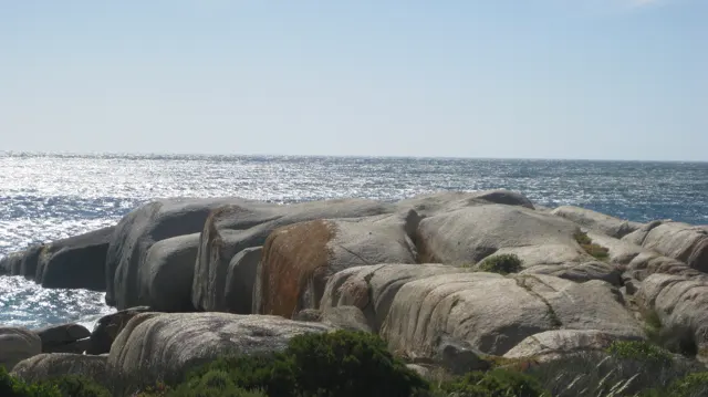 Rounded brown and grey boulders stand against a stretch of sunlit sea.
