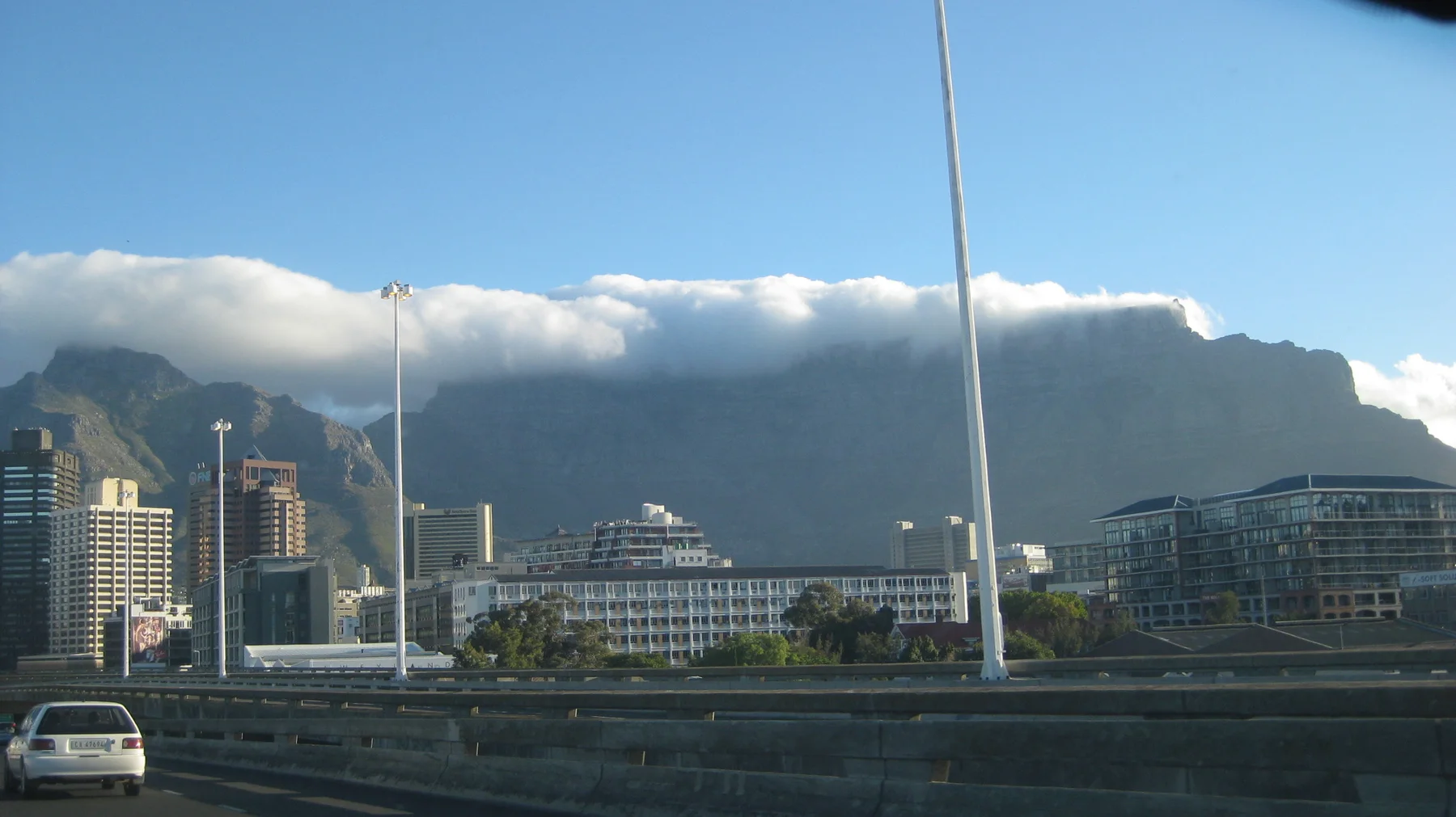 City buildings and a streetlight stand below a long mountain capped with cloud.