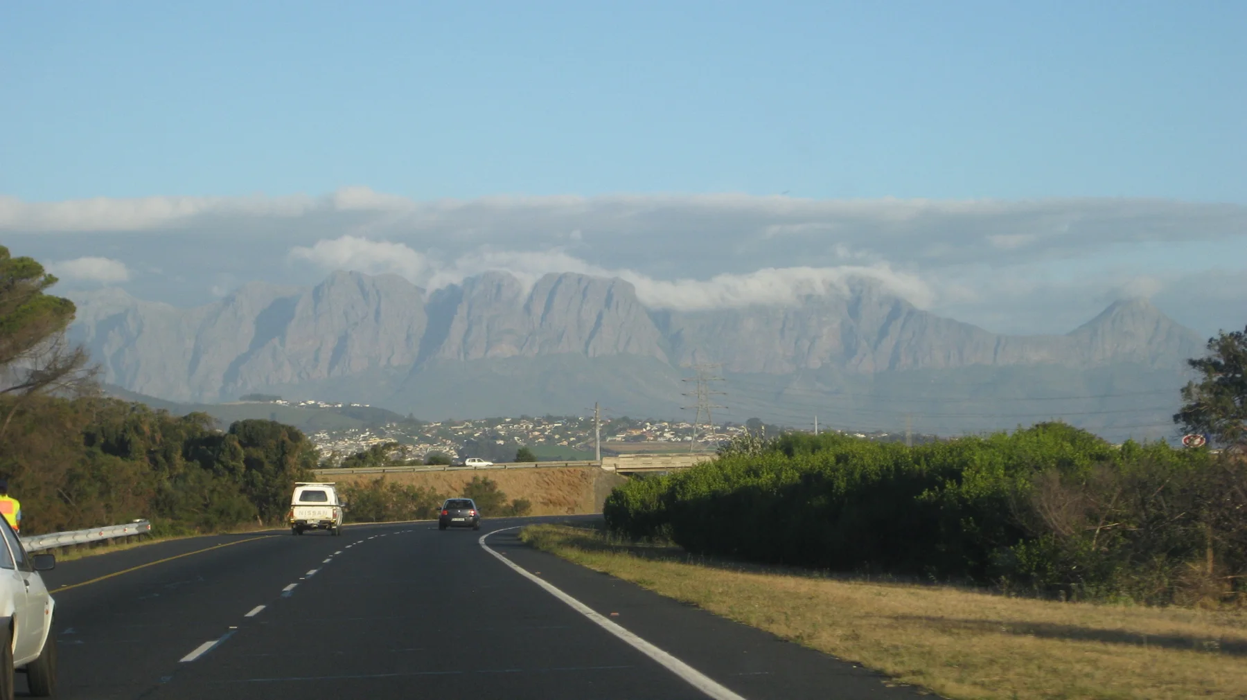 A white van travels down a road toward a long mountain covered with cloud.