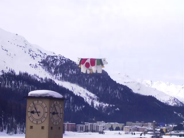 A snow-capped clock tower rises before wooded mountains and open white ground, with a colourful cow-shaped decoration above.