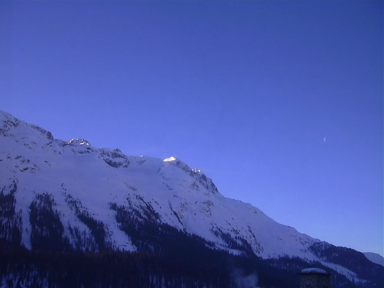 A snow-covered ridge slopes across the lower frame beneath a wide expanse of deep blue sky.