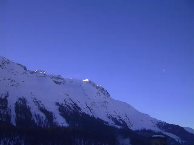 A snow-covered ridge slopes across the lower frame beneath a wide expanse of deep blue sky.