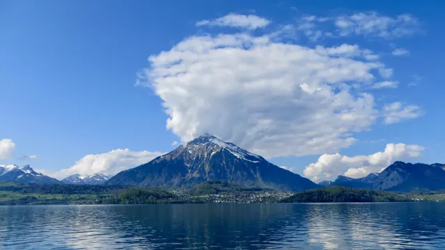 A white cloud rises above a mountain across the calm blue lake.