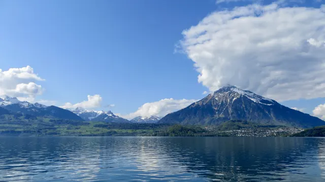 A mountain beneath a bright plume of cloud reflects in the lake.