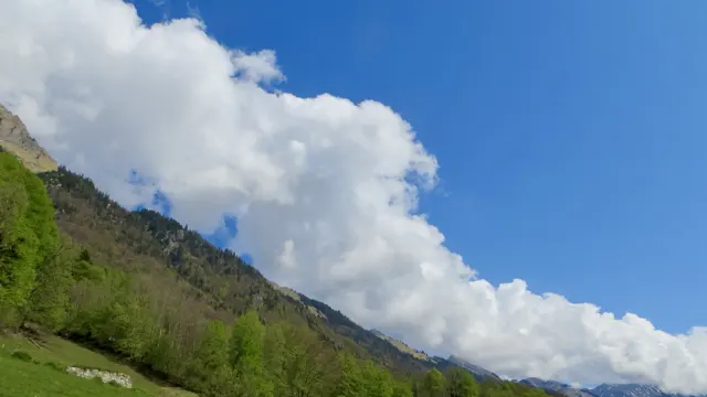 A green mountainside cuts diagonally beneath a towering white cloud.