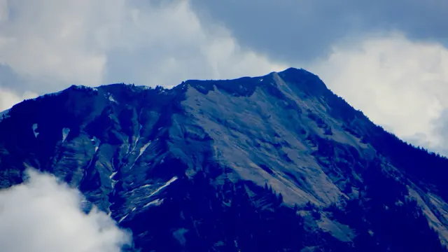 A dark, craggy mountain ridge emerges between pale clouds.