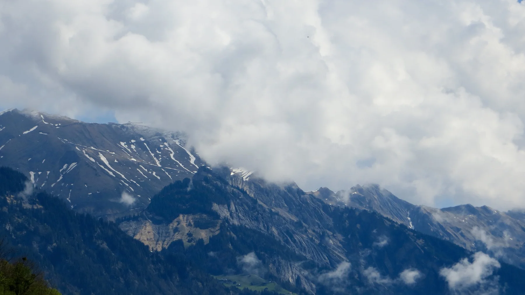 Clouds gather around a dark mountain streaked with snow.