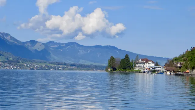 A tree-covered point and a pale building project into the lake below distant mountains.