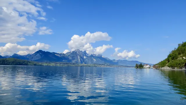 White clouds and distant snowy mountains reflect across a calm lake.