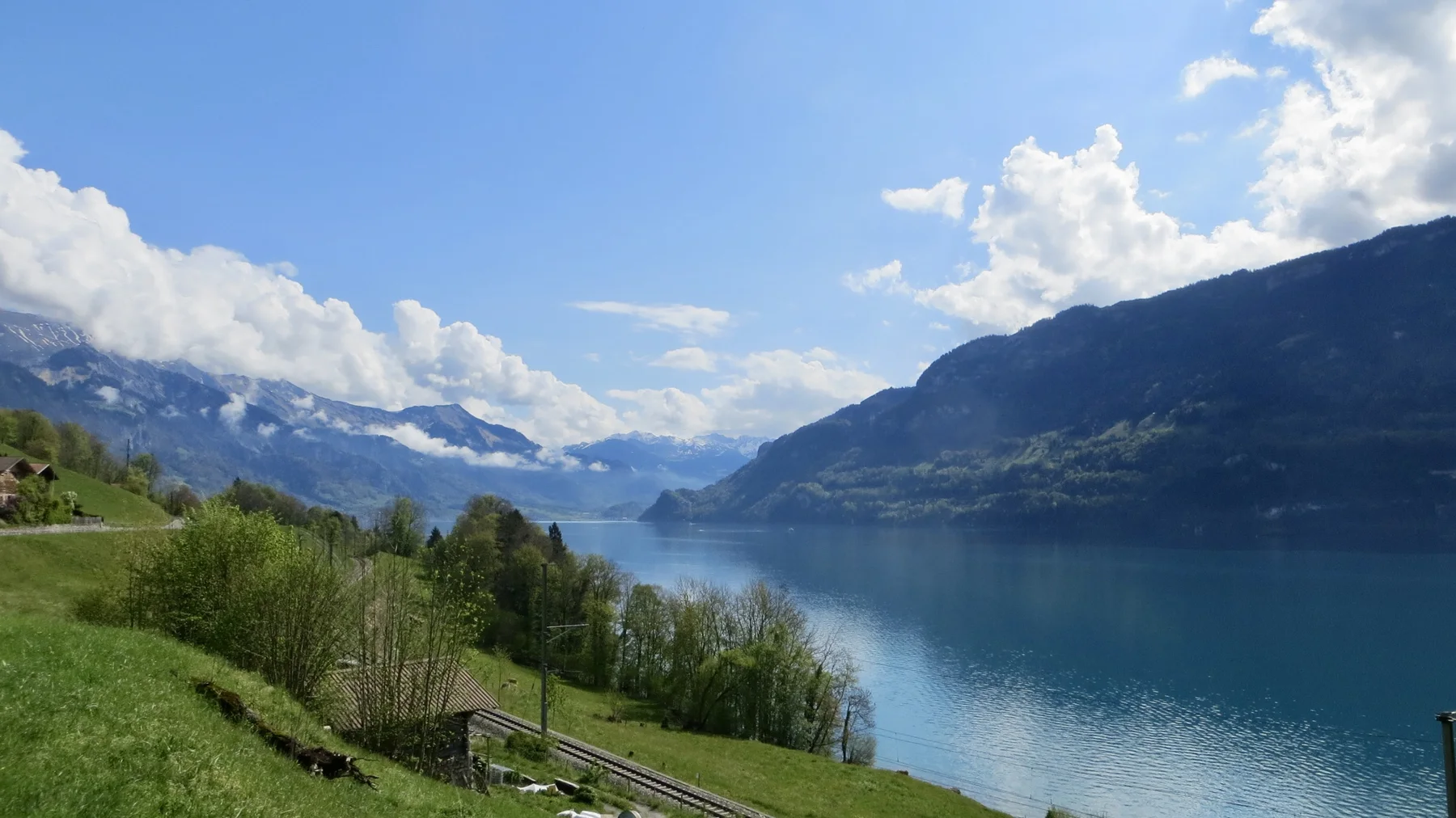 A narrow lake leads between green slopes toward a snowy mountain valley.