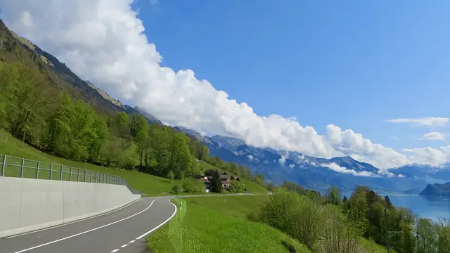 A curving road and concrete wall overlook the lake and green hillsides.