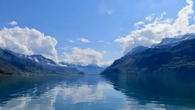 Mountains and clouds form a broad reflection along a quiet lake.
