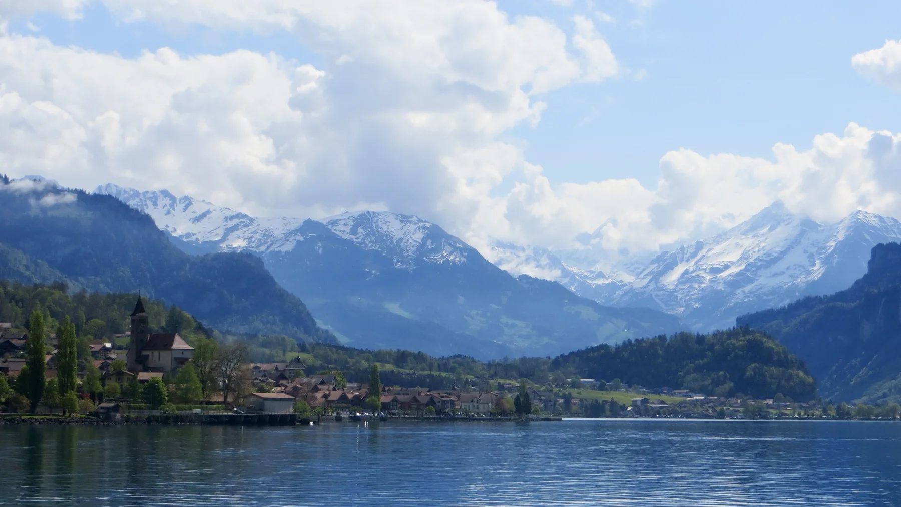 Lakeside buildings sit below mountains at the edge of still water.