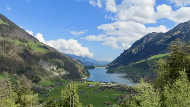 A long, narrow lake stretches beyond a village between steep green slopes.