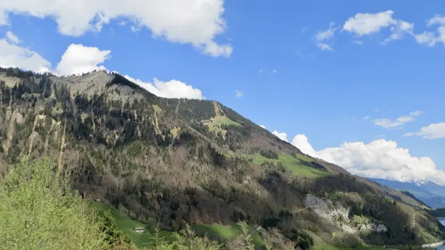 A rocky ridge descends toward green vegetation beneath a blue, cloud-filled sky.