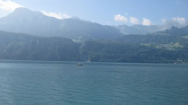 A small sailboat sits on blue water below hazy mountain slopes.