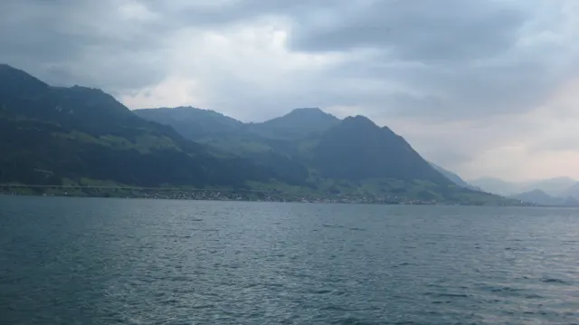 Clouds shade a long mountain shoreline above rippled lake water.