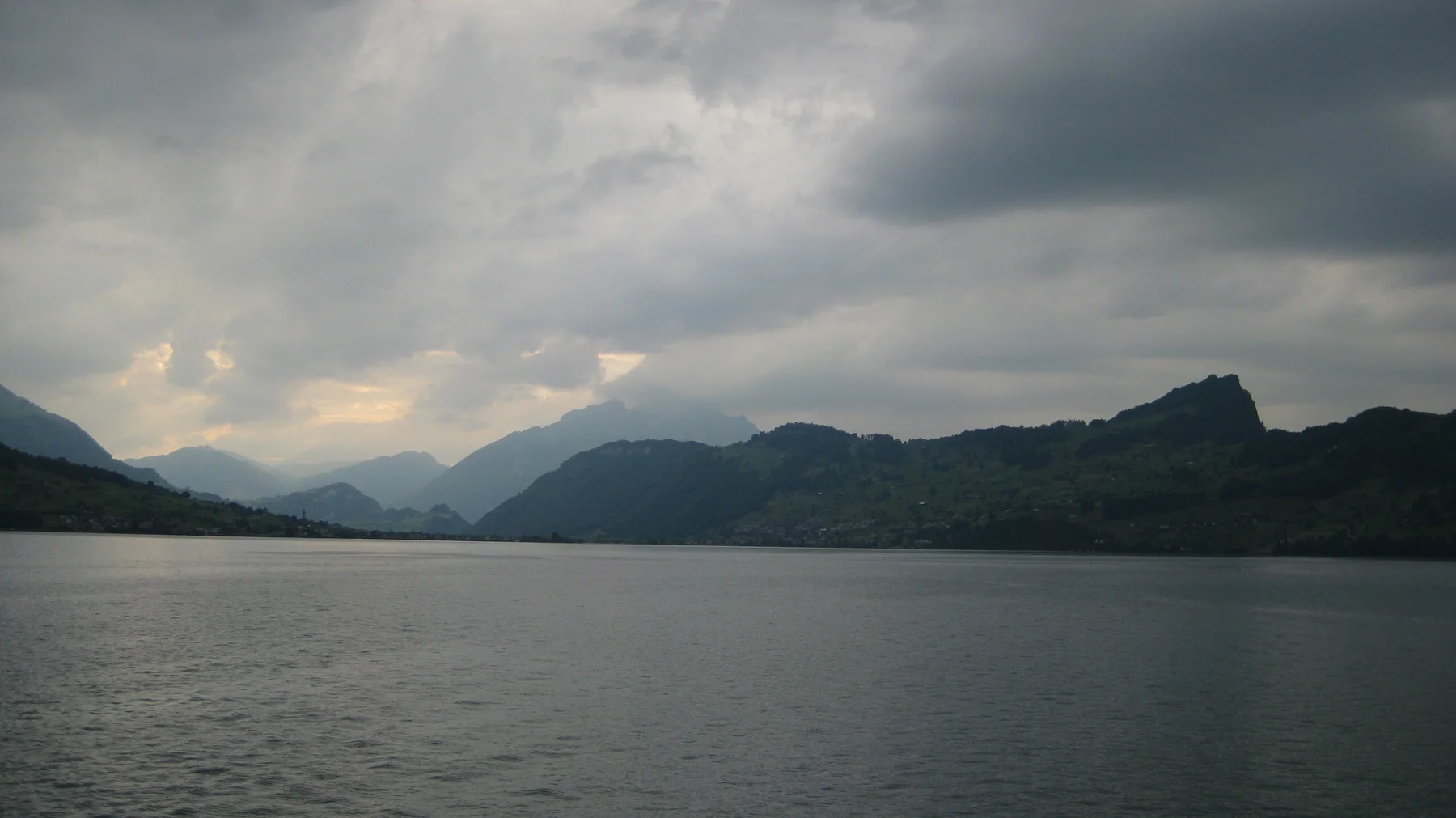 Layered mountains stretch beyond open lake water under a thick cloud ceiling.
