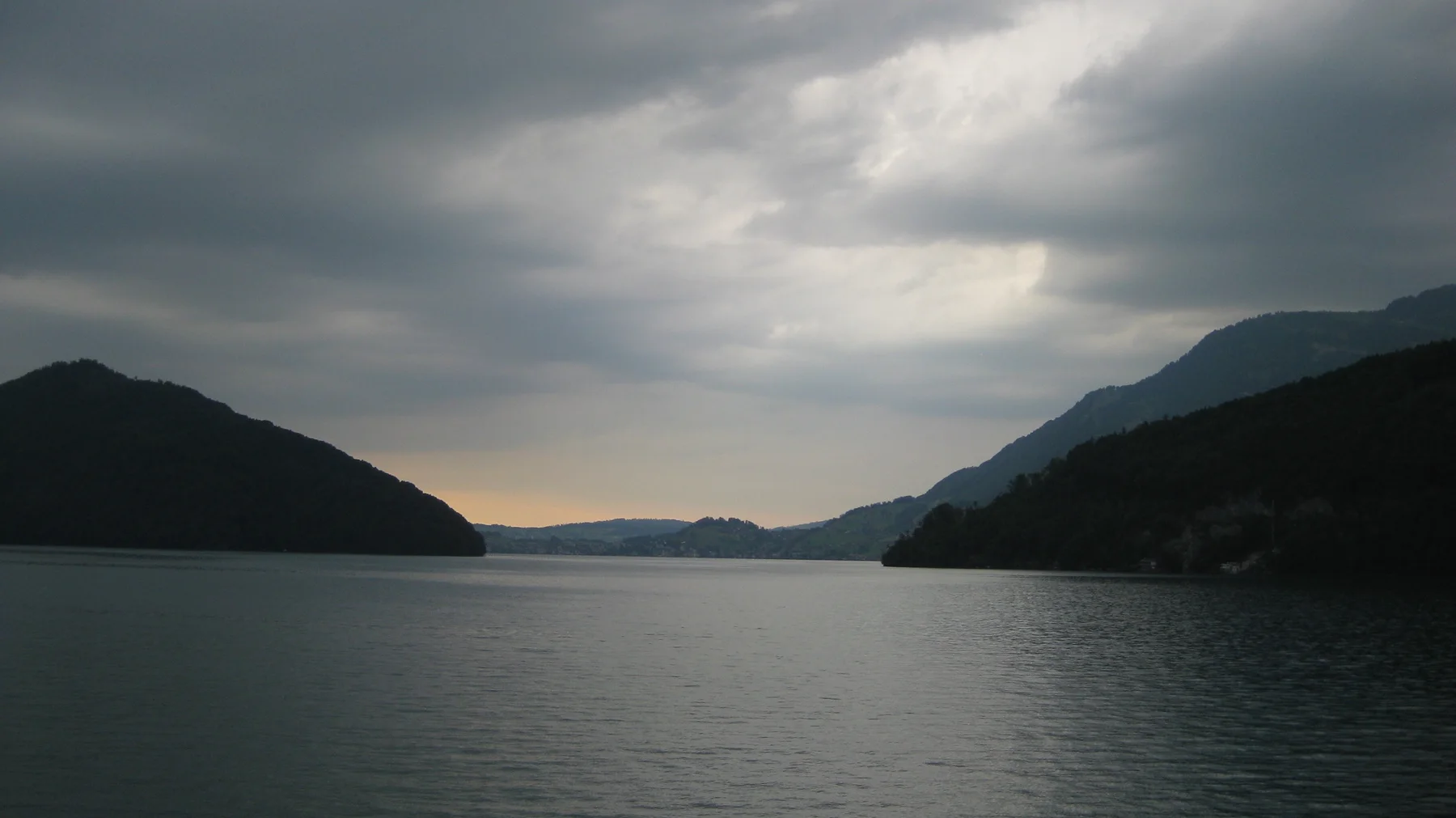 A narrow strip of warm light appears between dark hills across still water.