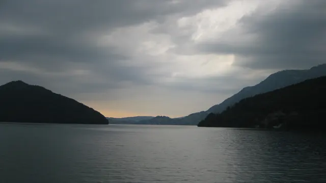 A narrow strip of warm light appears between dark hills across still water.