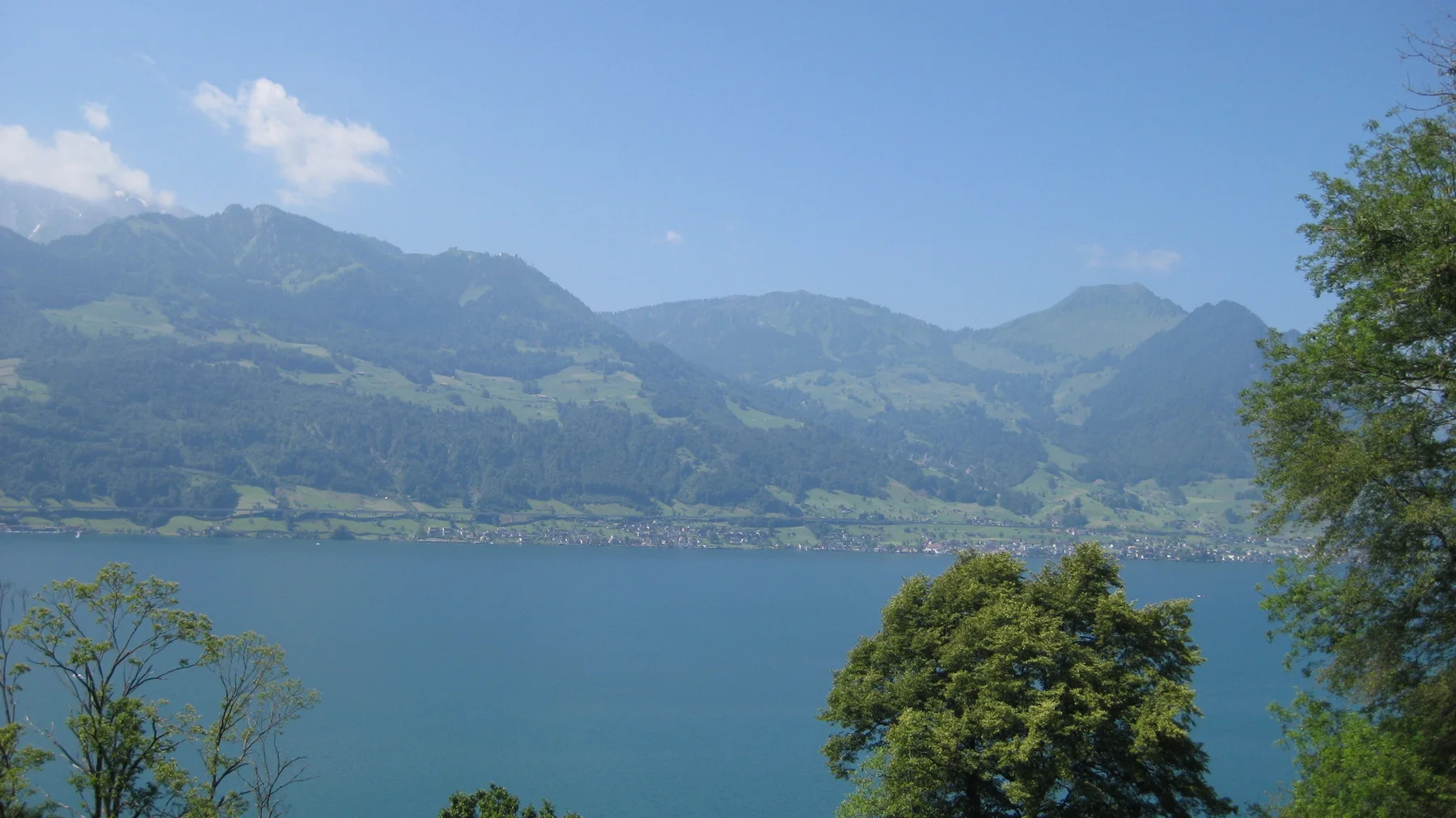 Green mountains and a line of shoreline buildings rise across bright blue water.