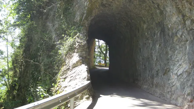 A narrow paved way passes through a short rock tunnel beside a railing.