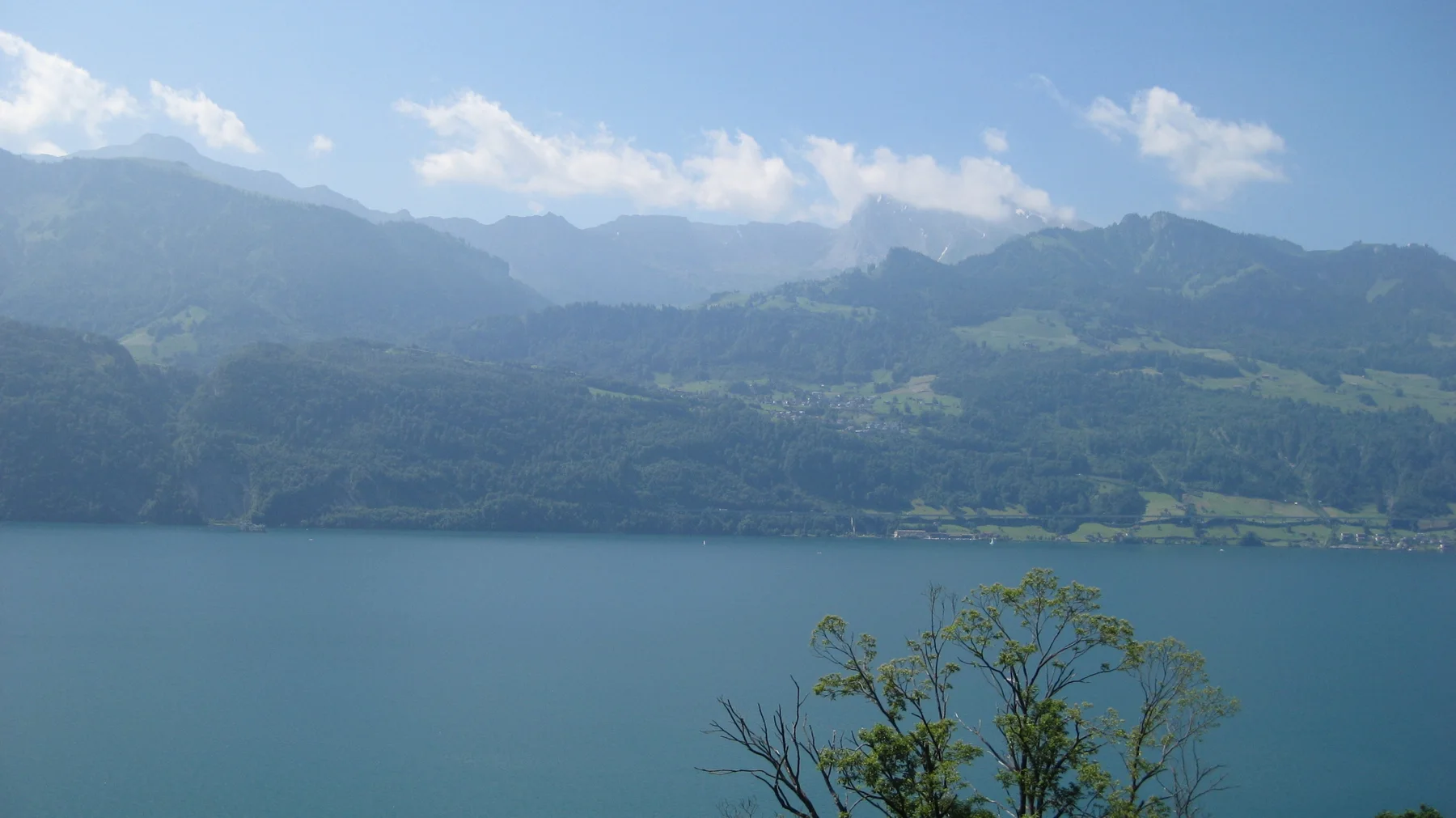 A broad lake stretches toward layered green mountains beneath scattered clouds.