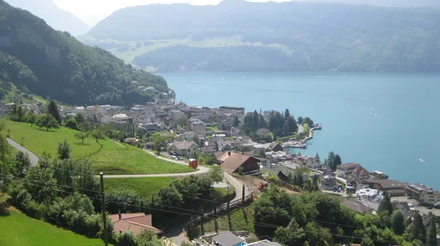 Green hillside fields overlook clustered buildings along a blue lake.