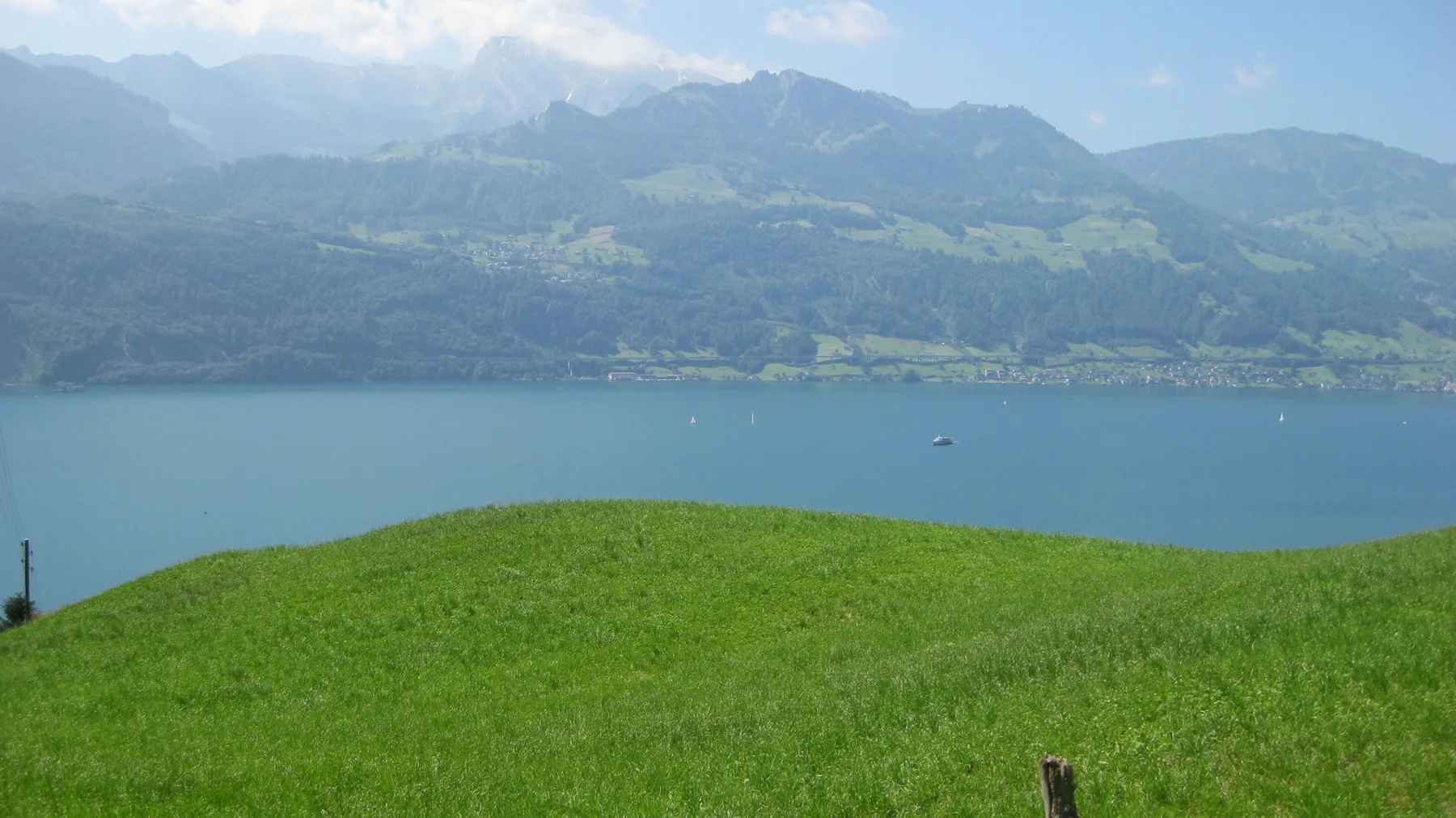 A rounded green meadow slopes toward a blue lake and distant mountains.