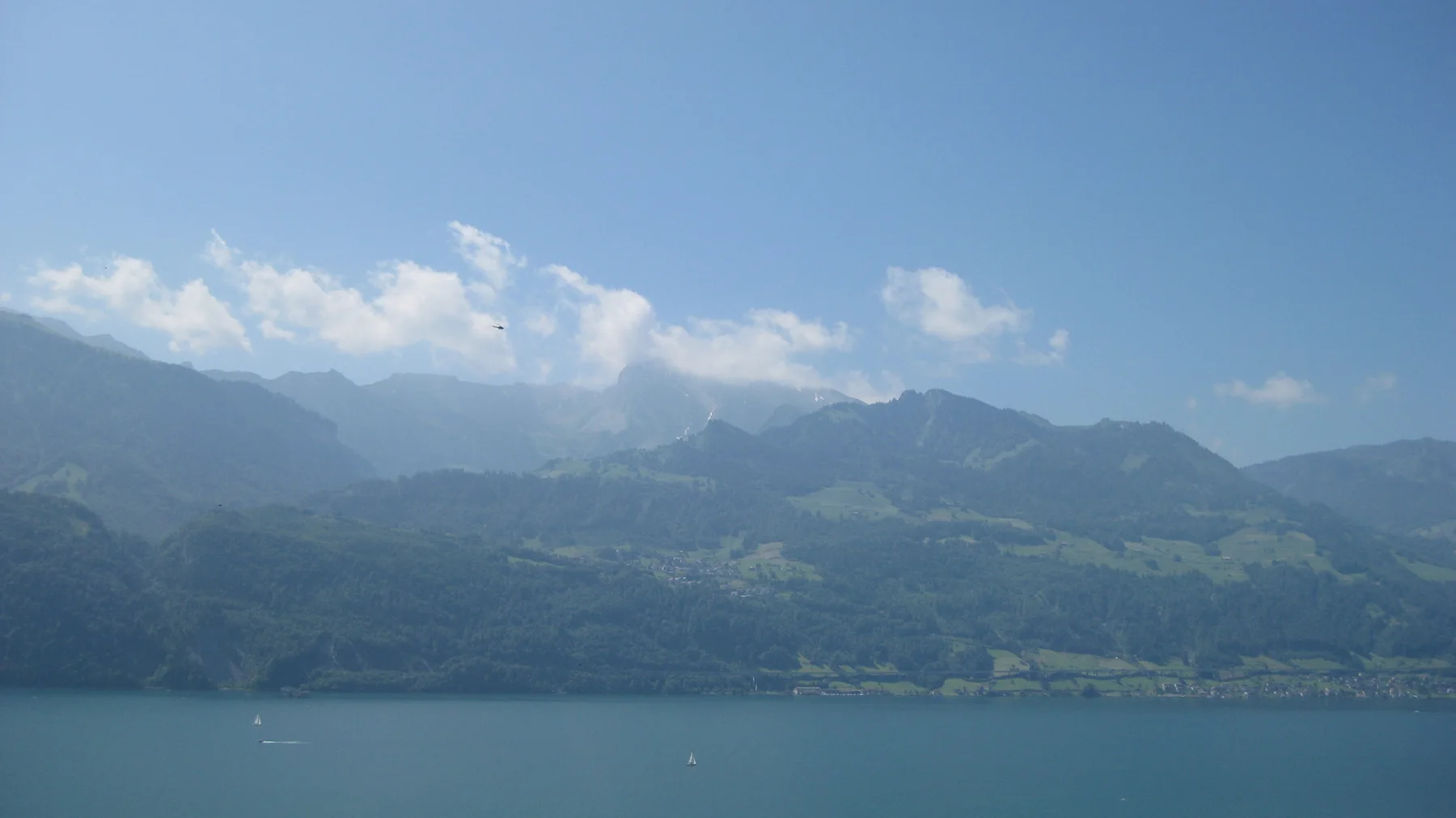 Small white clouds hang above a mountain range across a blue lake.
