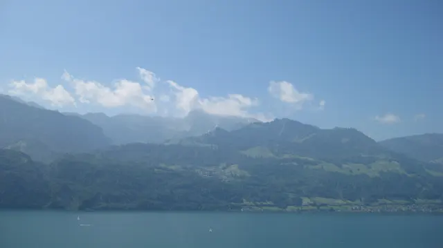 Small white clouds hang above a mountain range across a blue lake.