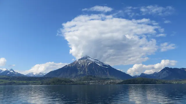 A large white cloud spreads above a snowy mountain reflected in blue water.