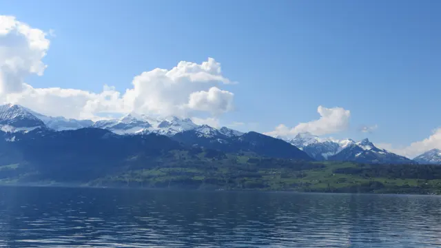 A snow-lined mountain range stretches across a rippled blue lake beneath white clouds.