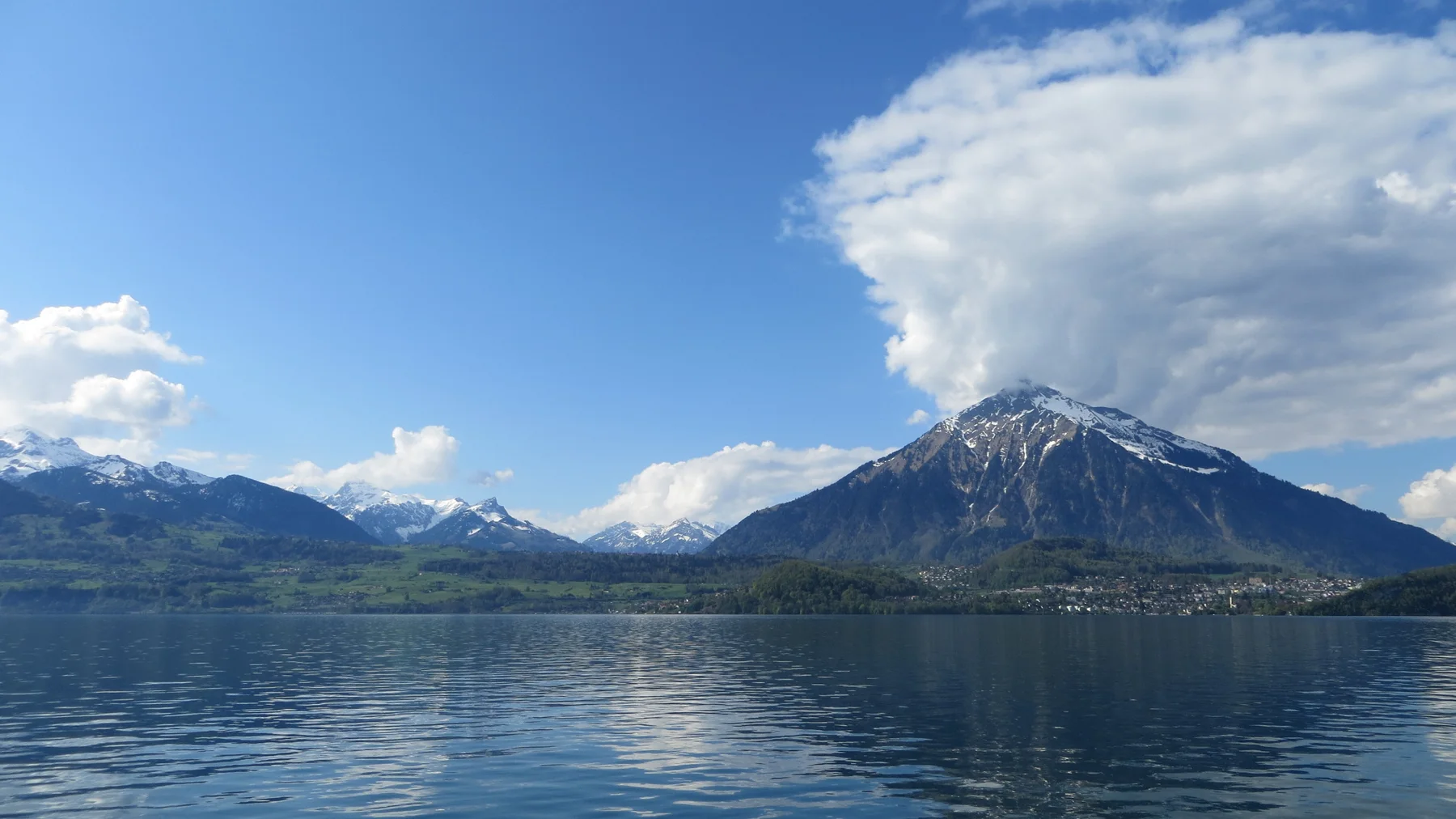 A pointed snowy mountain rises across the lake below a broad bank of cloud.