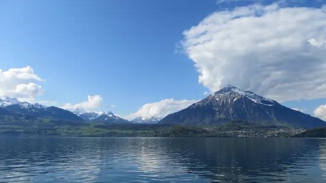 A pointed snowy mountain rises across the lake below a broad bank of cloud.