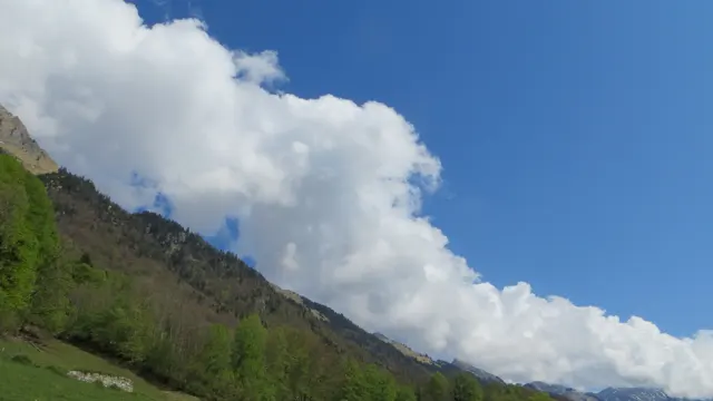 Bright white clouds follow a steep green and rocky mountainside.