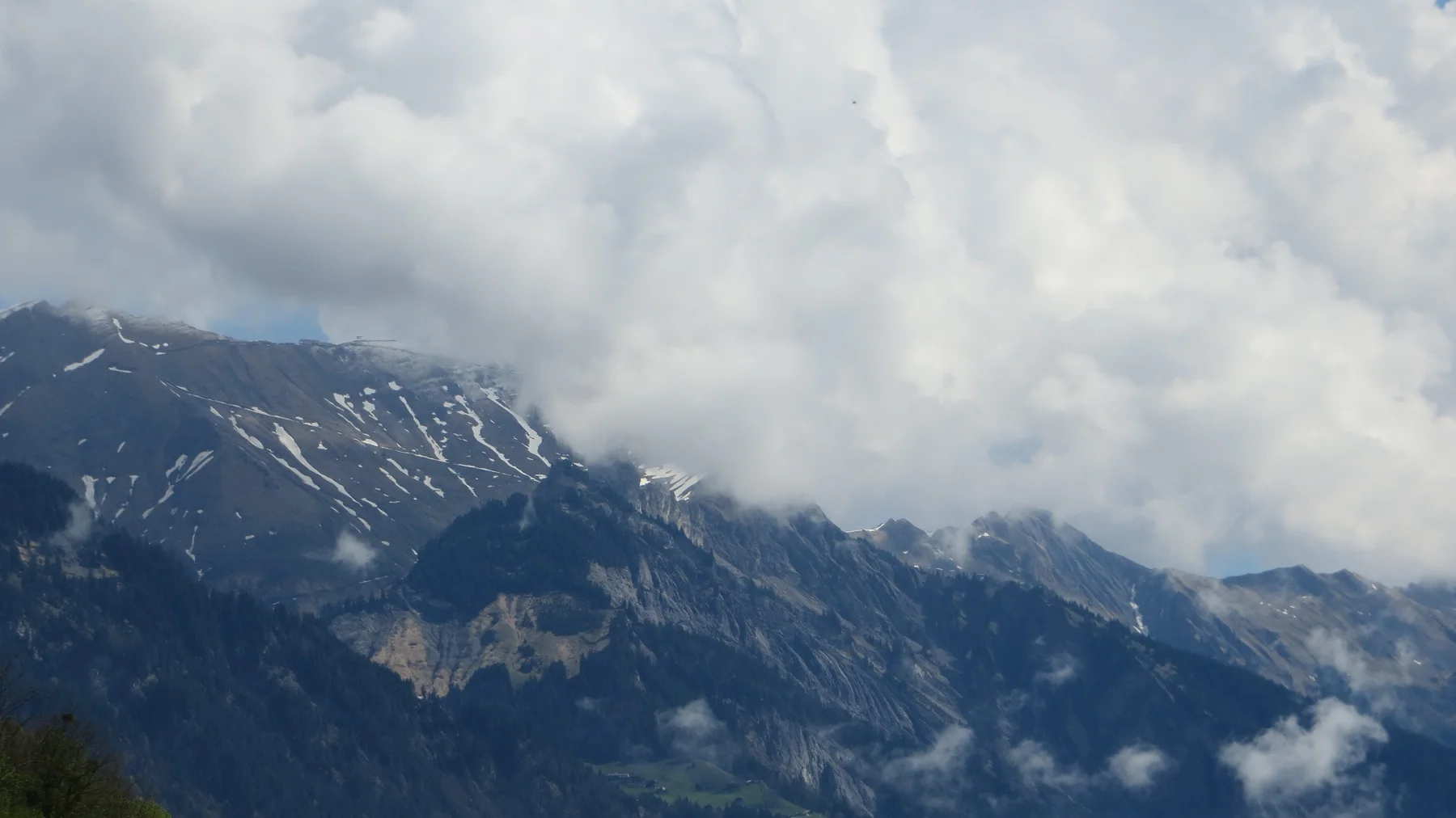 Thick clouds wrap around a dark mountain ridge streaked with snow.